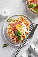 Cheese or potato savory waffles served with with tomatoes, cream cheese, ham and bazil leaves with cutlery. Delisious savory breakfast. Top view, flat lay
