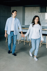 Fototapeta premium Attractive young woman and handsome man are enjoying spending time together while standing on light modern kitchen with cup of coffee in hands.