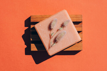 Handmade vegan soap bar with fragrant herbs on wooden soap dish over red brown background.Making...
