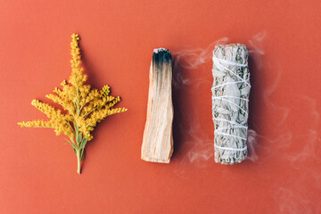 Burning incenseю White sage and palo santo stick with smoke over red brown background. Bundle for meditation and room fumigation. Selective focus. Flat lay style