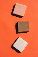 Handmade organic soap bars made with natural ingredients over red brown background. Making herbal soap at home. Flat lay style, mockup. Vertical composition