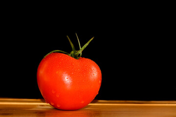 A tomato with drops on a wooden table. Vegatables. Vegetarian. Black background.	