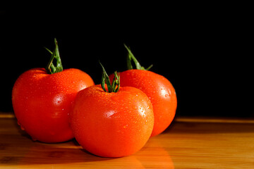 Three red tomatoes with drops on a wooden table. Vegatables. Vegetarian. Black background.