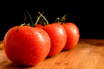 Three red tomatoes with drops on a wooden table. Vegatables. Vegetarian. Black background.