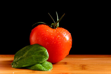 A tomato with drops and a basil leaf on a wooden table. Vegatables. Vegetarian. Black background.	
