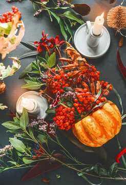 Autumn decoration arrangements with pumpkin, rowan berries and autumn leaves on dark table with candles, top view