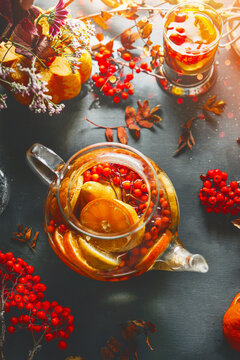 Class teapot with healthy vitamin tea with Rowan berries, orange and lemon slices on table with ingredients. Hot drink for cold autumn season. Close up