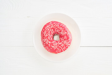 One pink donut, top view. Donut on a plate on white wooden table. Delicious breakfast, sweet donut with copy space..