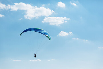 Blue Paraglider flying into the sky with clouds on a sunny day