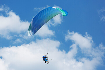 Blue Paraglider flying into the sky with clouds on a sunny day