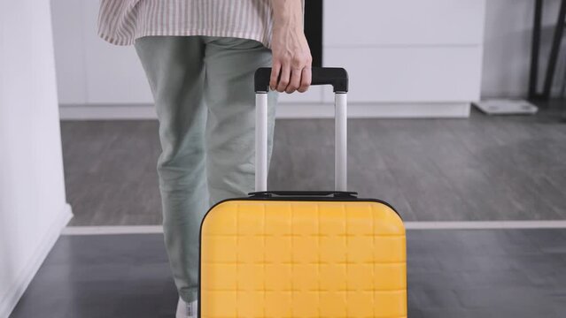 An unrecognizable woman with a yellow suitcase arrived at the rented apartment.