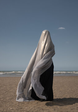 abstract portrait of woman in black dress on the beach hiding under thin veil