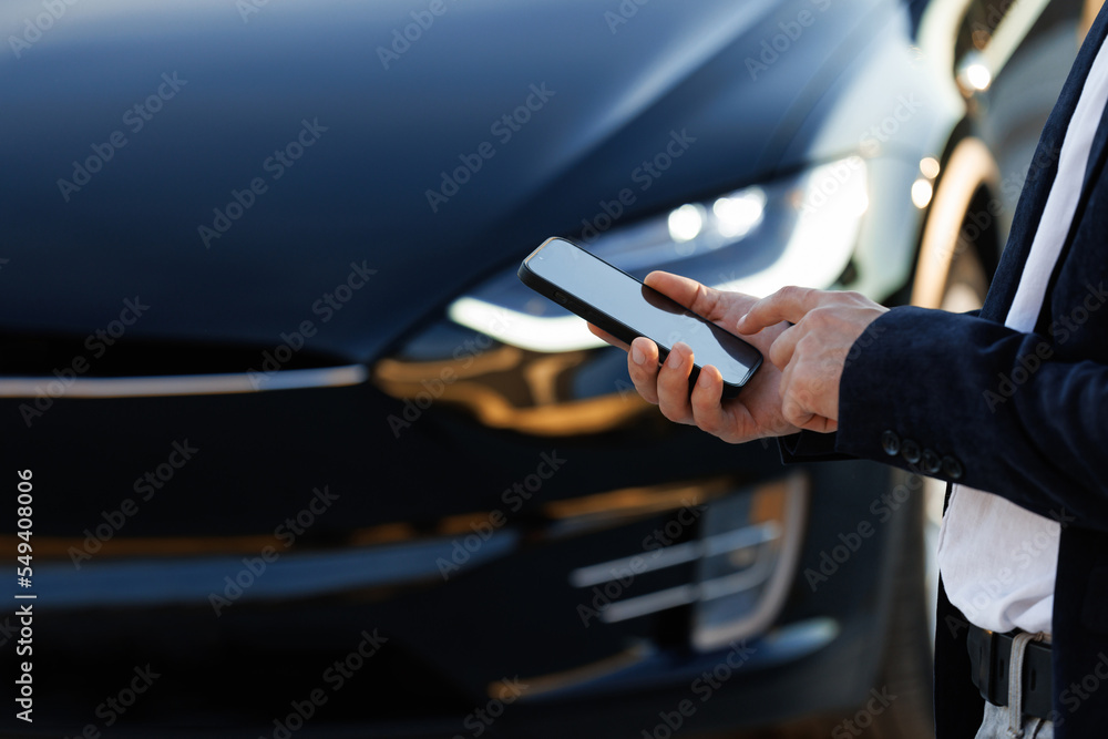 Wall mural unrecognizable elegant man using smartphone app for remote controlling of premium class tesla plaid 