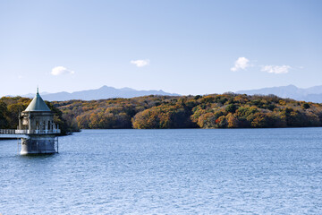 青空を背景に狭山湖の取水塔と紅葉の森
