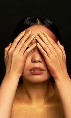 Fototapeta premium I don't see the evil. An Asian girl on a black background in a photo studio. Gold.