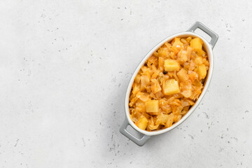 Vegan stewed cabbage potato in ceramic baking dish. Top view, copy space, flat lay.