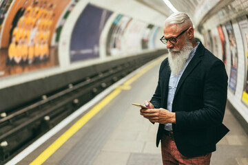 Senior hipster man using smartphone in subway underground - Main focus on hand holding mobile phone - obrazy, fototapety, plakaty