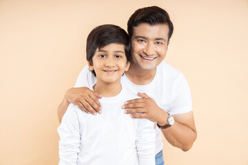 Happy young indian father with his son wearing white casual t-shirt standing over isolated beige...