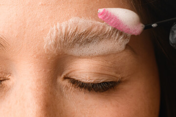 part of female face on the eyebrows of which cleaning foam applied with brush