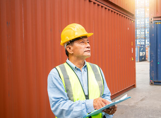 Professional senior male worker in helmet and uniform inspecting cargo at freight container shipping company before exporting to port.