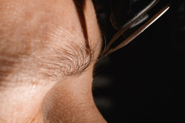 beautiful close-up on female eyebrows and steel tweezers plucking eyebrow hairs