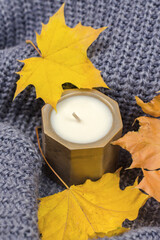 Candle in a concrete pot and yellow autumn leaves. Home autumn comfort