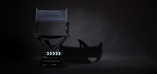 Back of black director chair and black clapper board on black background.