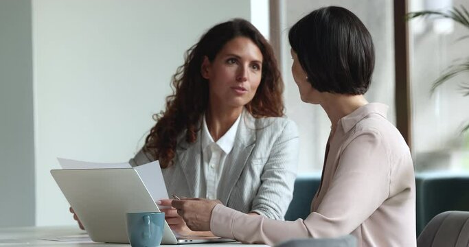 Teamwork, formal meeting with client in company office, consider agreement terms. Hispanic millennial and middle-aged women gather to discuss contract details, planning cooperation, work at workplace