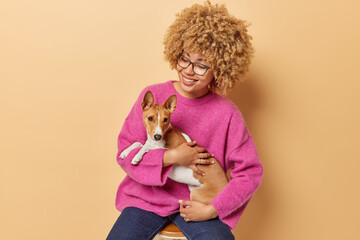 Happy curly haired woman embraces and take care of her favorite pet likes basenji dog enjoys...