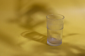 A glass kept on a yellow background with the shadow of a plant