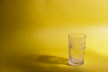 A glass kept on a yellow background with the shadow of a plant
