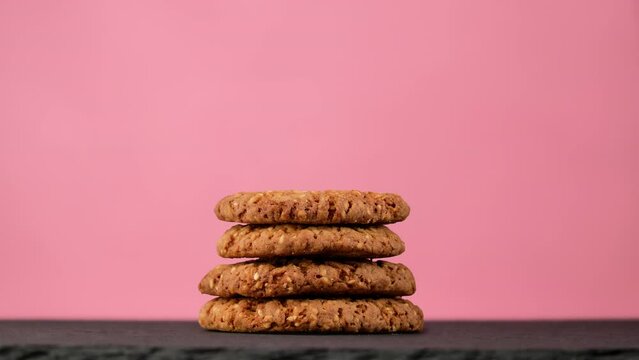 Stop motion of appearing and disappearing pyramid of homemade cookies with sesame seeds. Stack of oatmeal cookies on pink background. Tasty dessert
