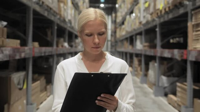 A professional worker, a woman in a white shirt with documents in her hands, checks stocks at a retail warehouse. Concept delivery, Distribution center. Front view, a woman moving towards the camera