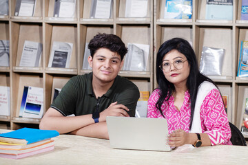 Obraz premium Young indian student boy and female teacher using laptop studying in college library with bookshelf behind. working on assignment or project.