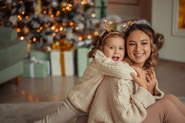 Fototapeta premium Happy New Year! family traditions. young mother and her daughter have fun at home near the Christmas tree and fireplace