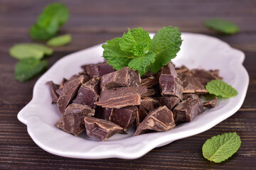 Pieces of dark chocolate on a white porcelain plate on a wooden background.
