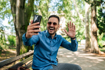 Happy young adult handsome man, holding phone, waving, taking a picture.