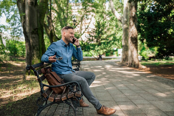 Handsome adult man, talking on his phone, holding sunglasses outside.