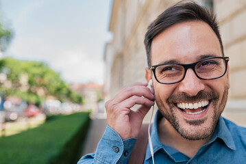 Portrait of smiling young adult man, putting earphones on, listening to music.