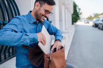Satisfied handsome adult businessman, packing his laptop in his handbag.