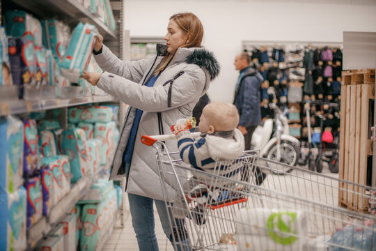 Young mother with baby son shopping in supermarket. A young mother chooses baby food with her baby sitting in a grocery cart. Close up. The concept of family shopping.
