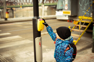 A little boy presses the yellow button of a pedestrian crossing and waits for the green light of the traffic light
