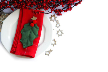 Festive table setting for Christmas with red berries decoration, White ceramic plate. Holly leaves and red tablecloth on a white background 