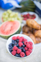 Summer picnic with watermelon, croissants, berries and baguette on a white blanket
