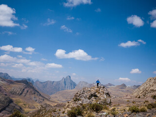 Hombre caminando sobre una roca hacia una gran montaña de rocas con un cielo nublado, llevando puesto una casaca o chamarra color azul, en Perú Sudamérica
