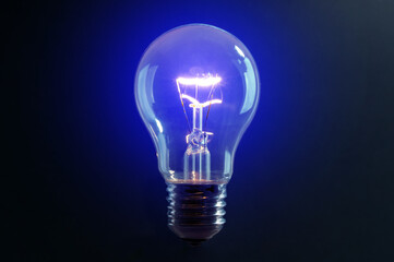 Old vintage light bulb glowing blue light on black background