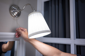 Male hand turn off the light on wall lamp in bedroom. Saving electricity energy at night. Switch...