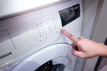 Male hand pushing button adjusting mode on white washing machine. Home appliance for laundry