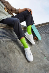 The legs of a skater boy sitting and wearing sneakers with penny skateboard © Nikolai