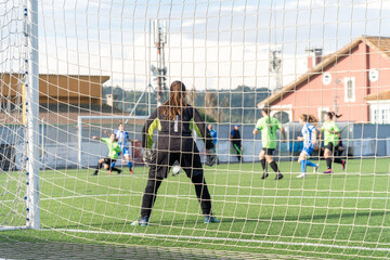 Female goalkeeper standing on goal. Unrecognizable female soccer players playing a game on the...